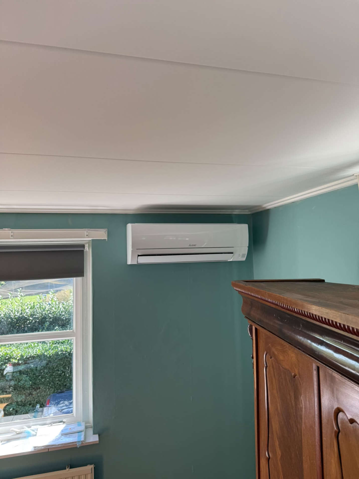 Mitsubishi Electric wandmodel boven het raam in een slaapkamer met groene wand