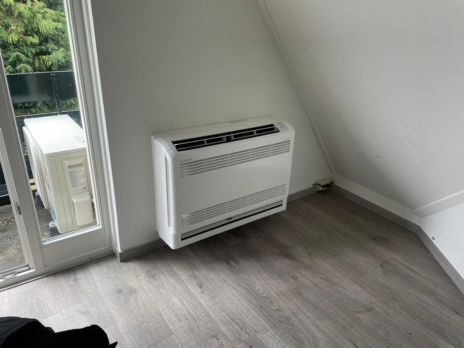 Wit vloermodel onder een schuin dak, buitenunit op het balkon
