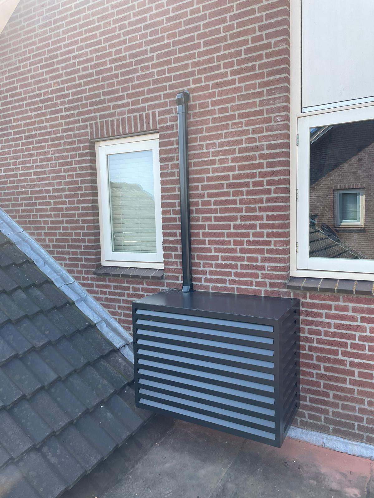 Antraciet airco-omkasting op het dak naast de gevel