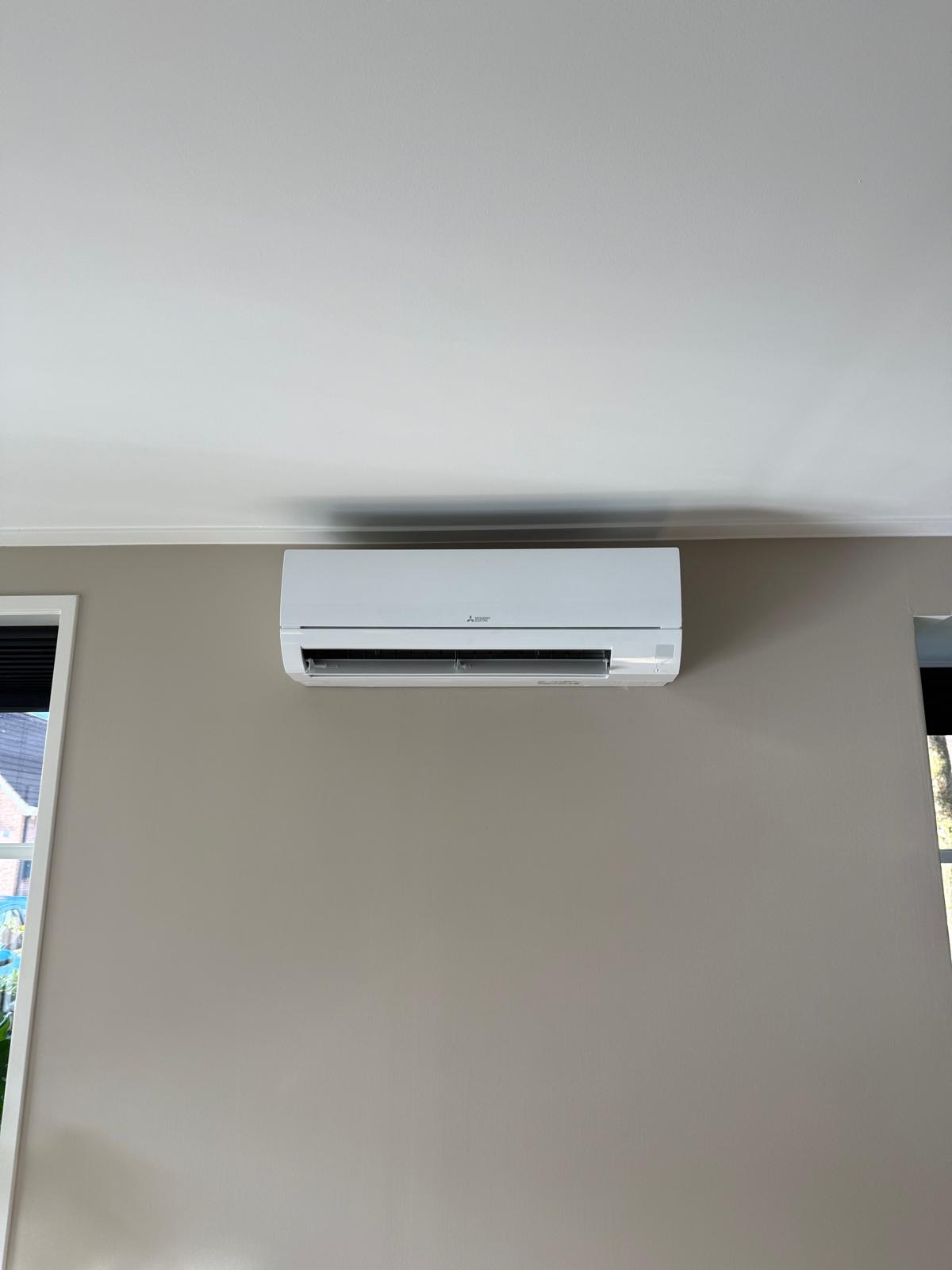 Witte Mitsubishi Electric binnenunit strak onder het plafond op een beige wand
