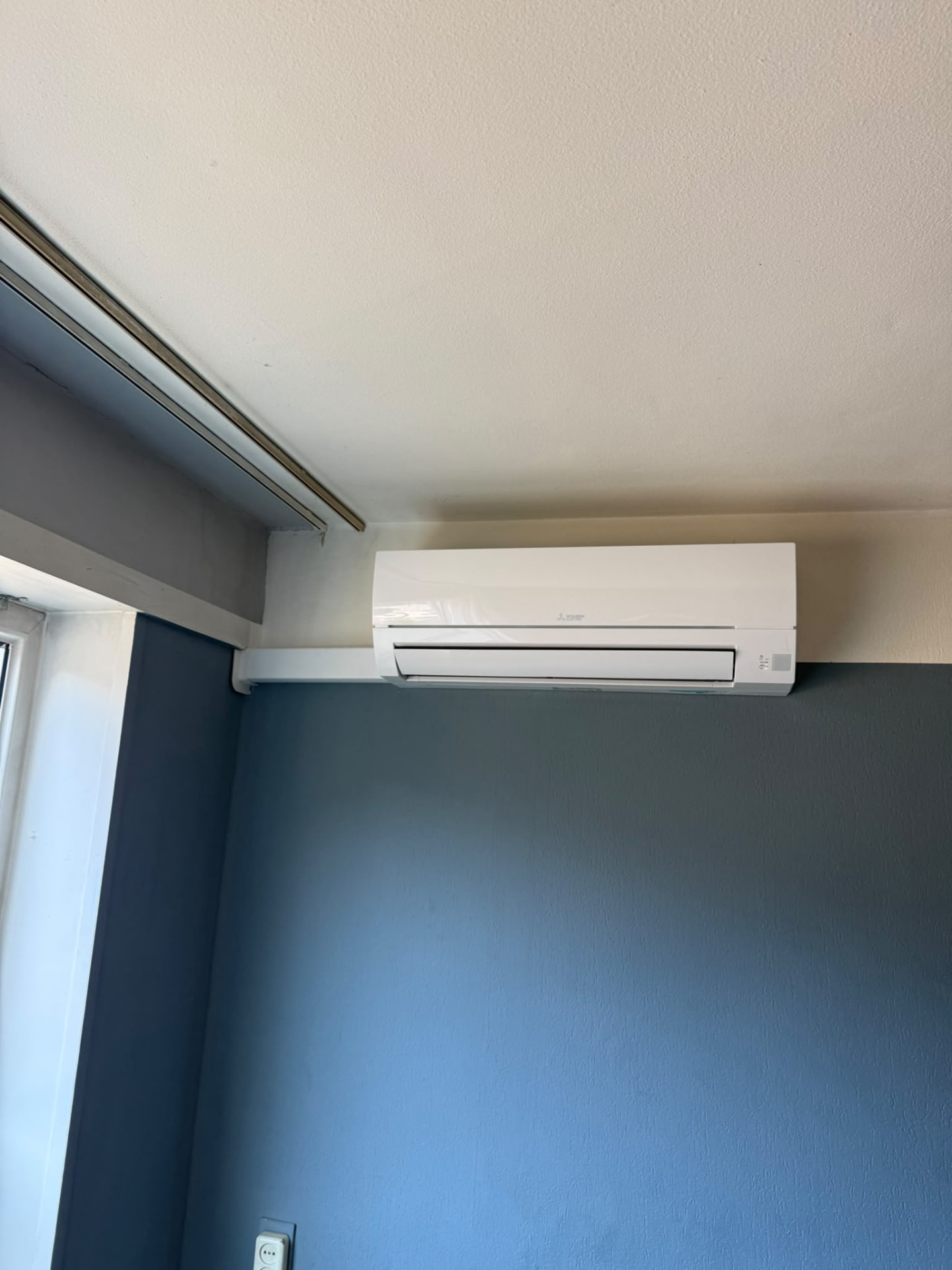 Mitsubishi Electric wandmodel met witte leidinggoot op een blauwe wand